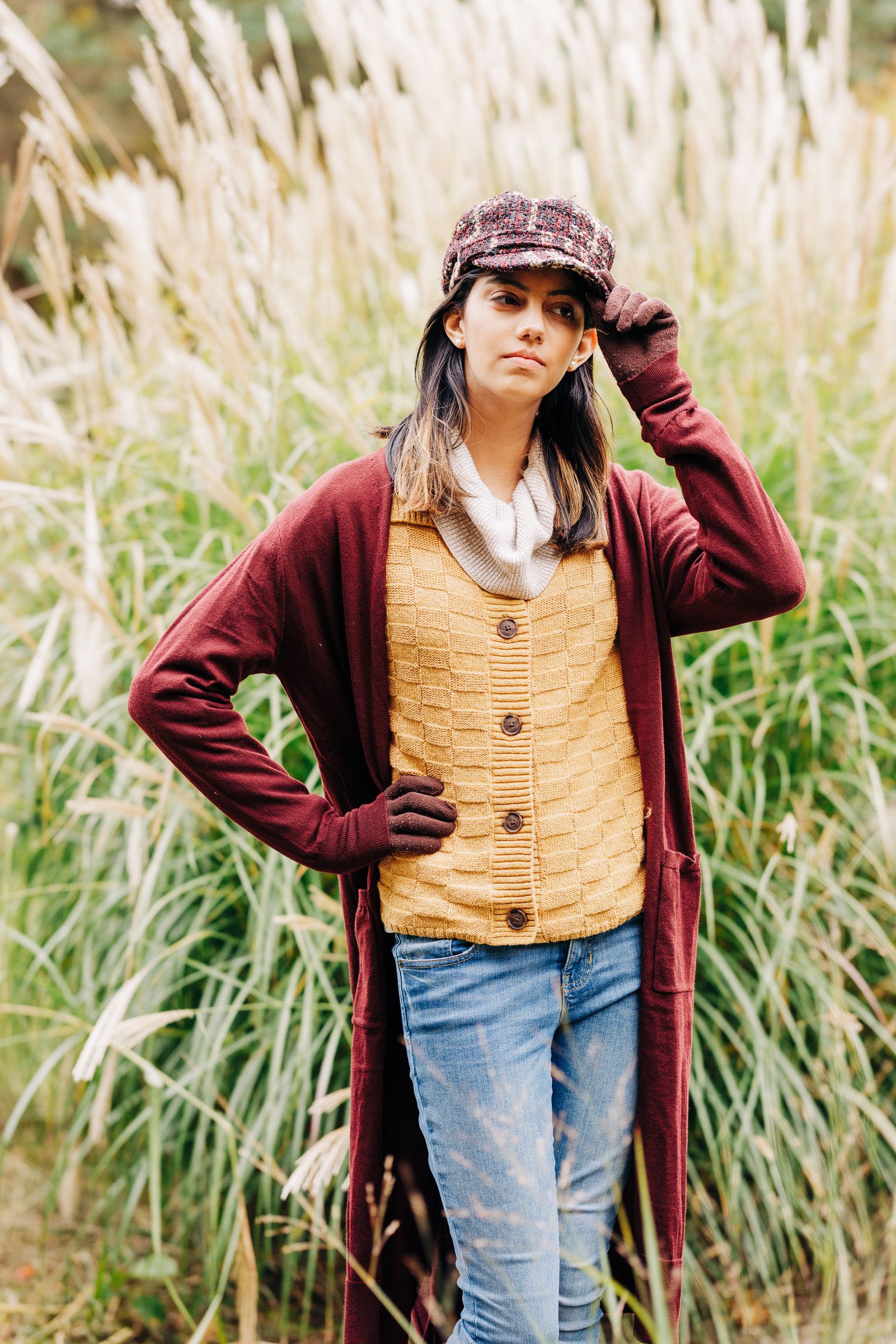 Senior standing in tall grass in a cardigan and hat