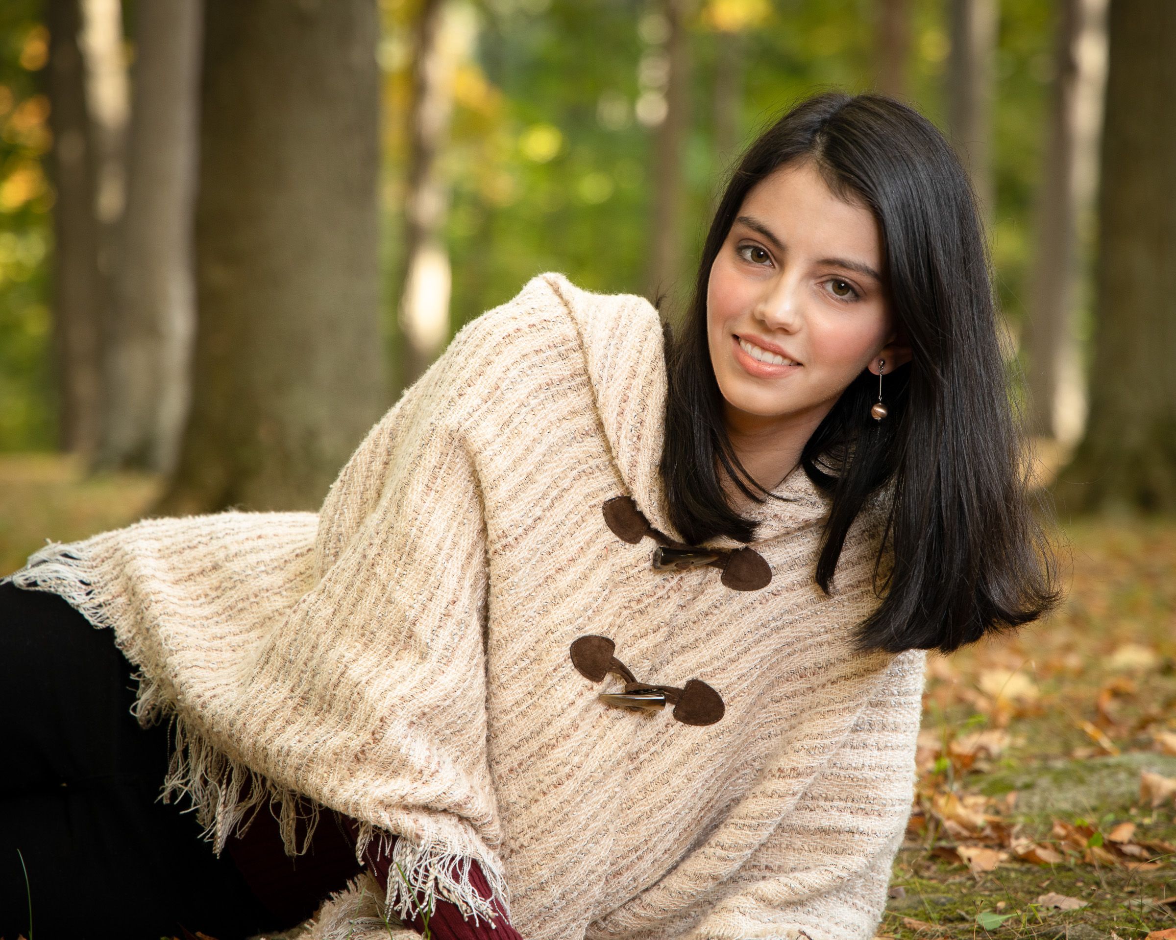 Senior relaxing on fall leaves in a cream sweater